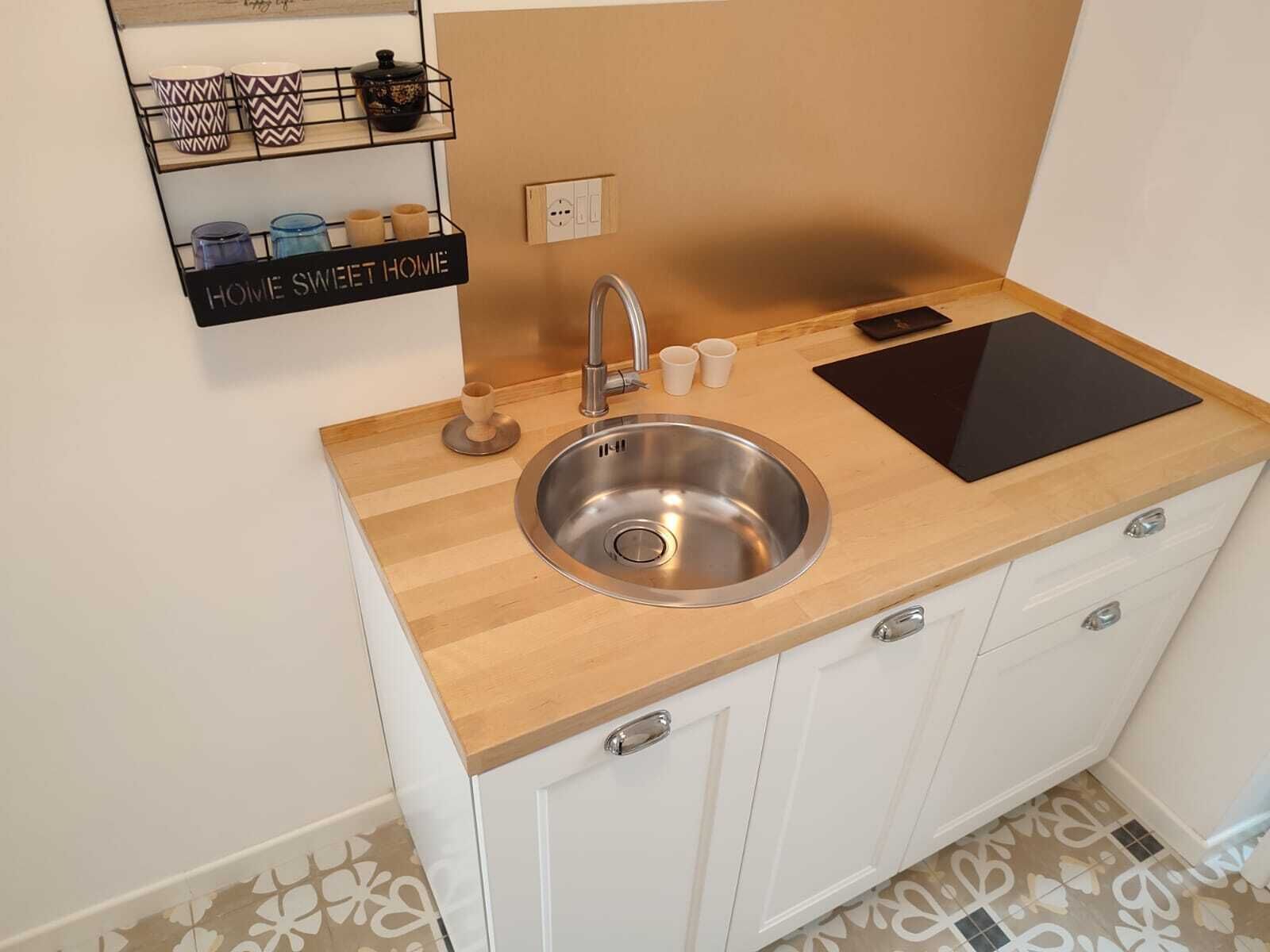Una cocina moderna con un lavamanos de acero inoxidable, encimera de madera y armarios blancos.