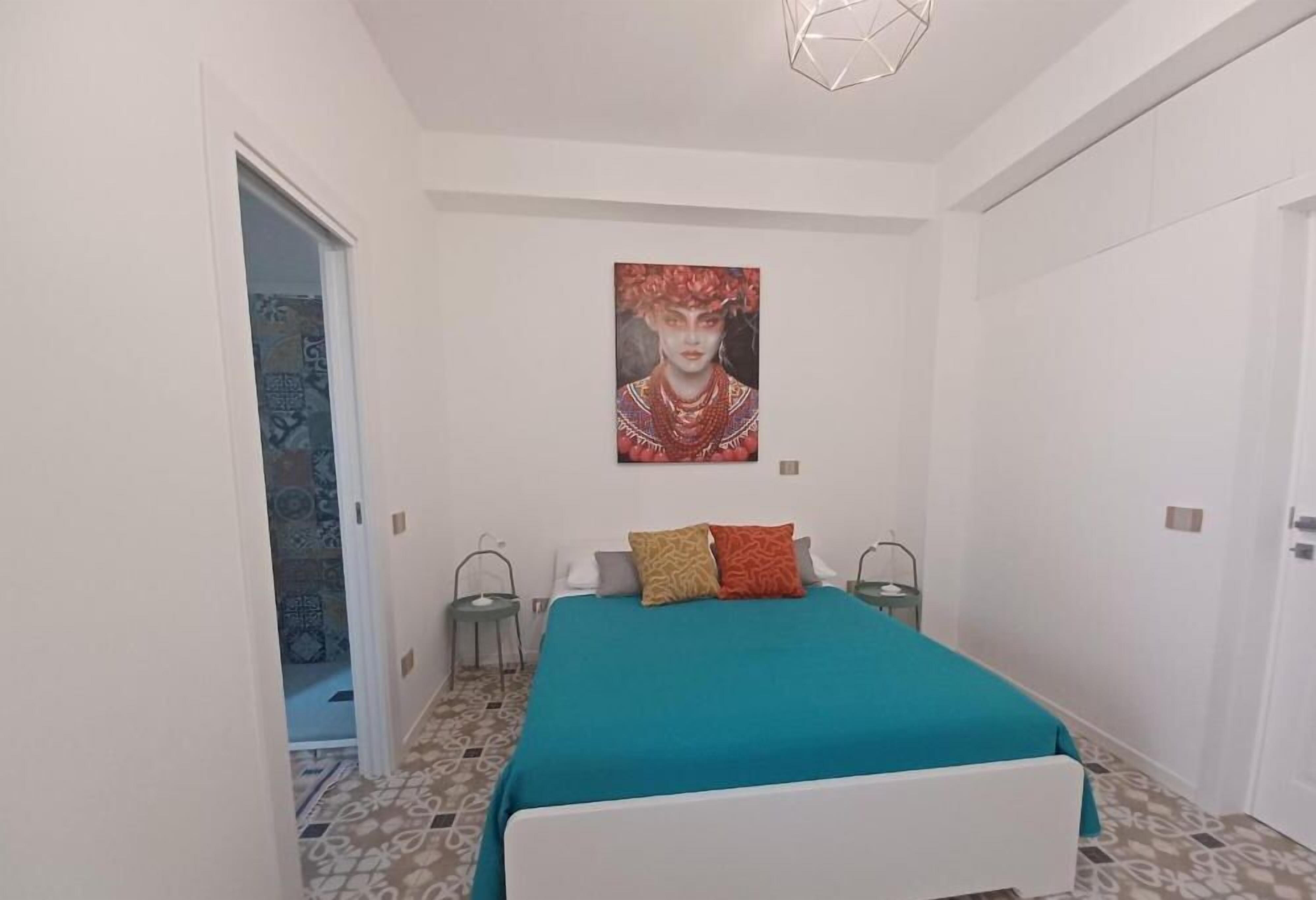 A bedroom with a bed, a painting on the wall, and a patterned floor.
