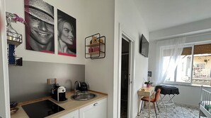 Cocina moderna con un lavamanos, cafetera y una pequeña mesa con una silla. Hay objetos decorativos en la pared y una ventana con vistas al exterior.