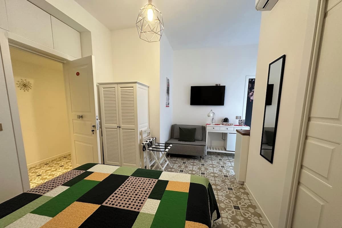 A bedroom with a bed, a desk, a chair, a wardrobe, and a TV.