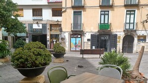 Un área de café al aire libre con mesas y sillas, rodeada de plantas en macetas y un banco.