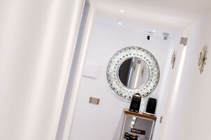 A white wall with a decorative mirror, a small shelf with a book titled '1001 Film', and a wall-mounted light fixture.