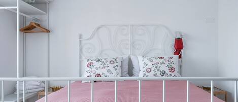 Estructura de cama metálica blanca con un colchón rosa texturizado, dos almohadas florales y un cabecero blanco.