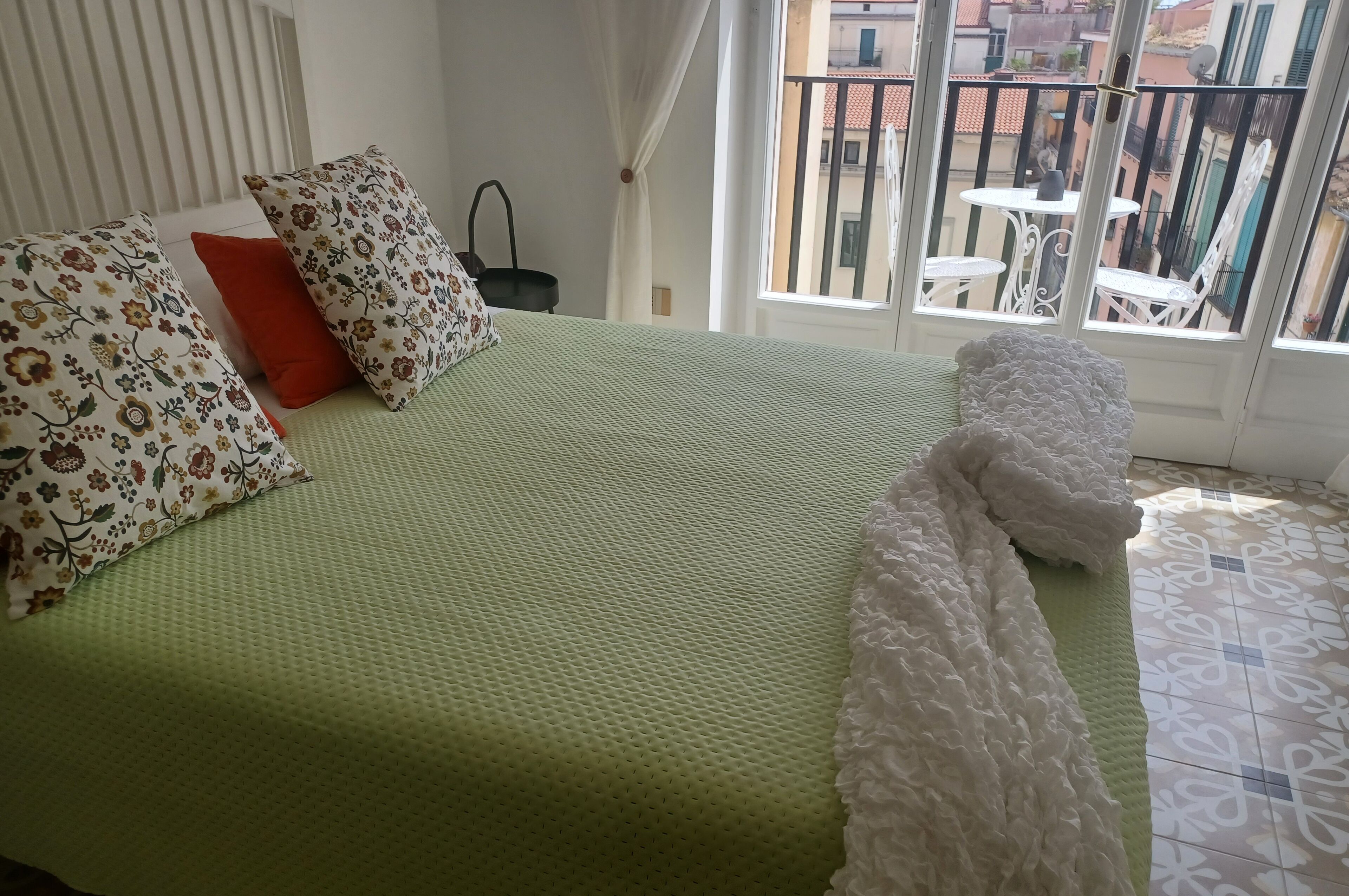 A bed with a green quilt, floral pillows, and a white blanket.