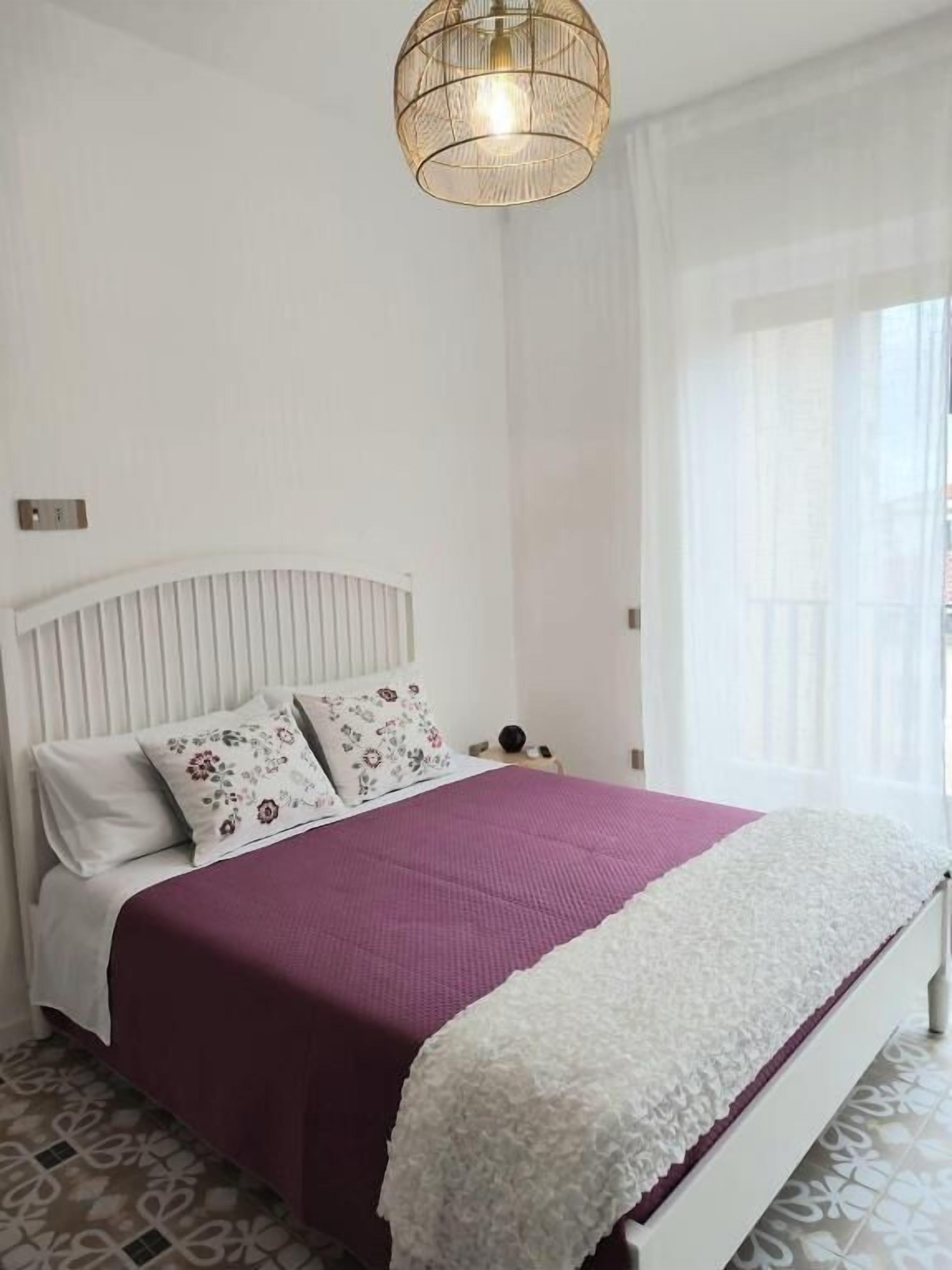 A neatly arranged bedroom with a bed, pillows, a bedside table, and a hanging light fixture.