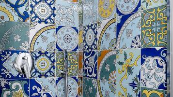 A bathroom with a tiled wall featuring a variety of blue, yellow, and white patterns.