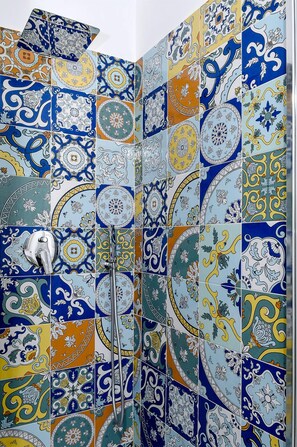 A bathroom with a tiled wall featuring a variety of blue, yellow, and white patterns.
