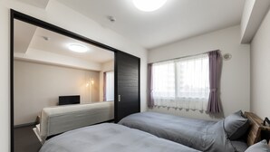A bedroom with two beds, a large mirror, a window with curtains, and a ceiling light. - STARGAZE 602 (Sapporo)