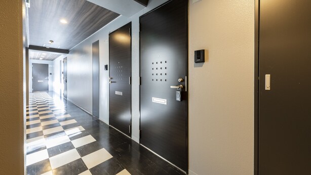 A hallway with checkered flooring, two doors with keypads, and a nameplate on the right door. - STARGAZE 602 (Sapporo)