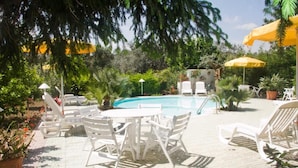 A pool area with white lounge chairs and a table, surrounded by potted plants and umbrellas. - Hotel Sporting (Vasto)