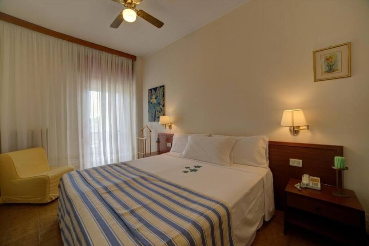Une chambre d’hôtel avec un lit, une chaise, une table de chevet avec une lampe et un ventilateur de plafond.