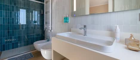 Un baño moderno con cabina de ducha de vidrio, un lavabo blanco y un espejo grande.