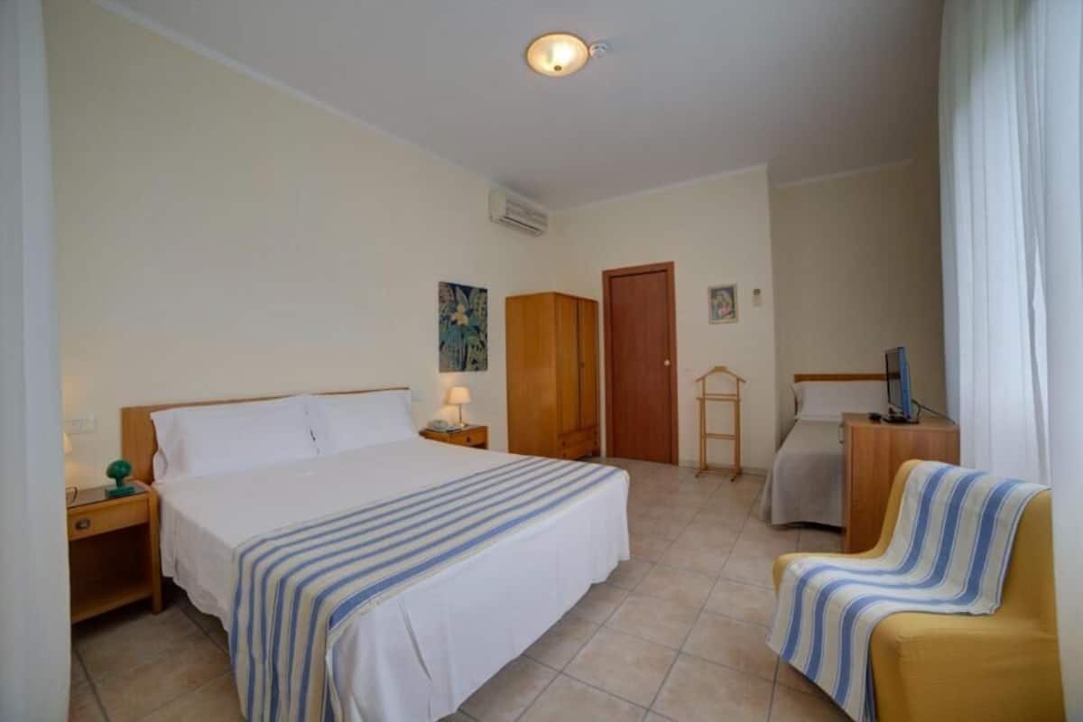 Une chambre d’hôtel avec un grand lit, une chaise, un bureau, une armoire et un téléviseur.