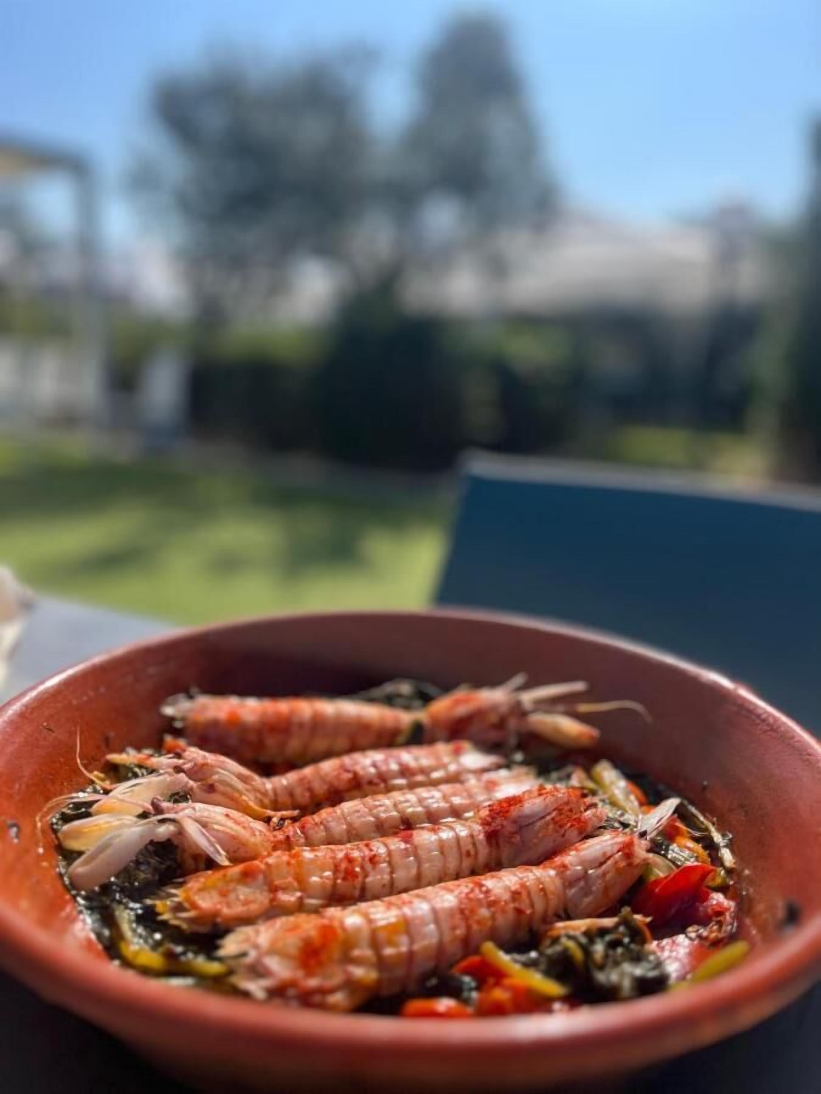 A terracotta bowl containing cooked shrimp with vegetables.