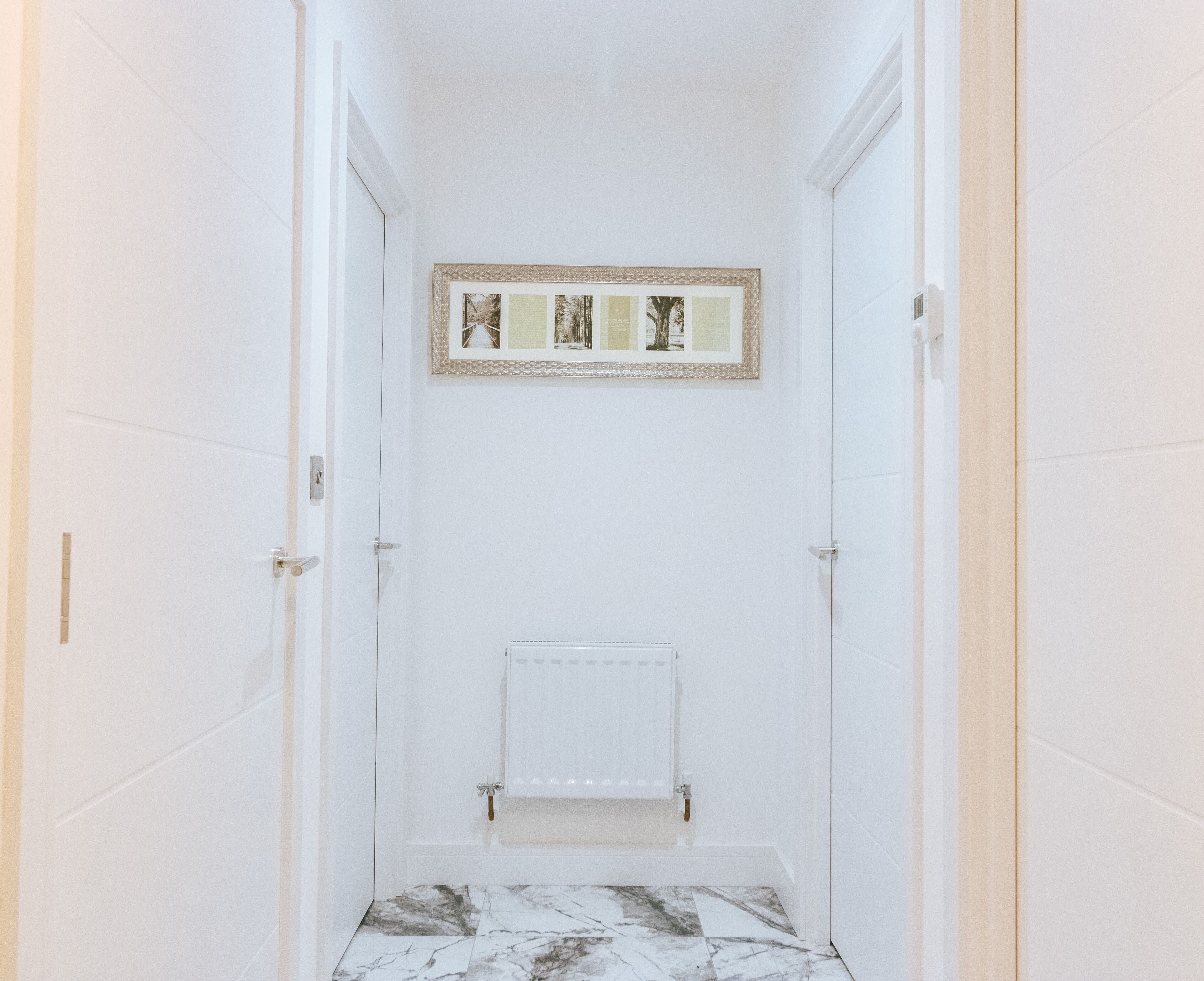 A bathroom with white walls, a marble floor, a framed picture on the wall, and a white radiator.