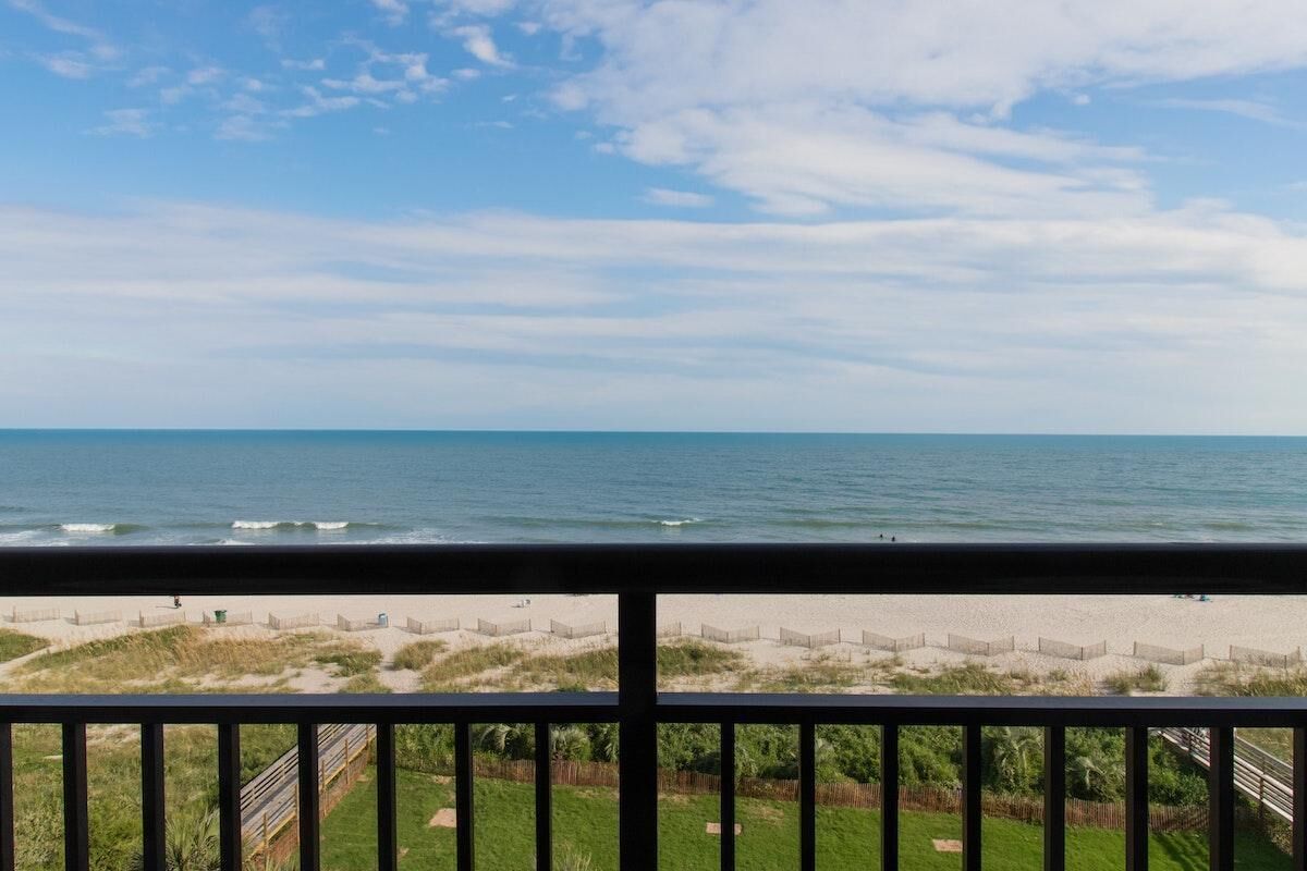 A beach view from a balcony with a railing, sandy beach, and ocean.