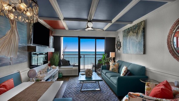 A living room with a view of the ocean, a ceiling fan, and a large painting on the wall.