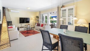 Un salon moderne avec un canapé, une table à manger et des chaises. Un téléviseur est fixé au mur et il y a une fenêtre avec des rideaux.