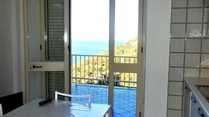 A small kitchen with a dining table and chairs, a view of the sea through an open door, and a tiled backsplash. - I FIORI DI DONNA ESTER (Pisciotta)