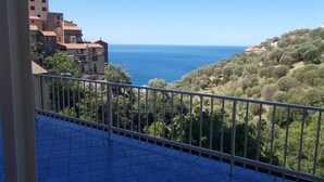 A balcony with a tiled floor and metal railing, overlooking a coastal area with buildings and trees. - I FIORI DI DONNA ESTER (Pisciotta)