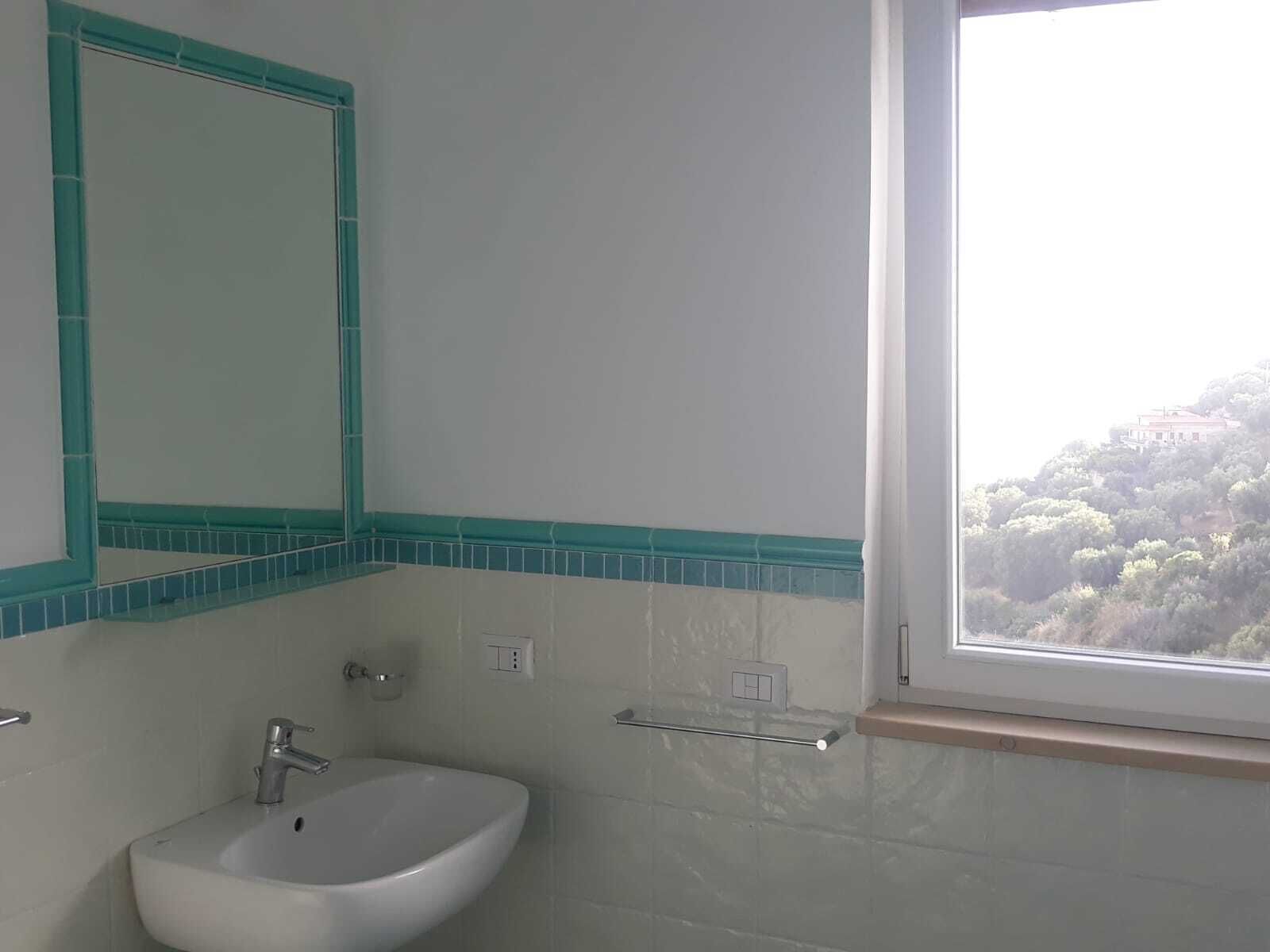 A bathroom with a white sink, a mirror, and a window with a view of a hill.