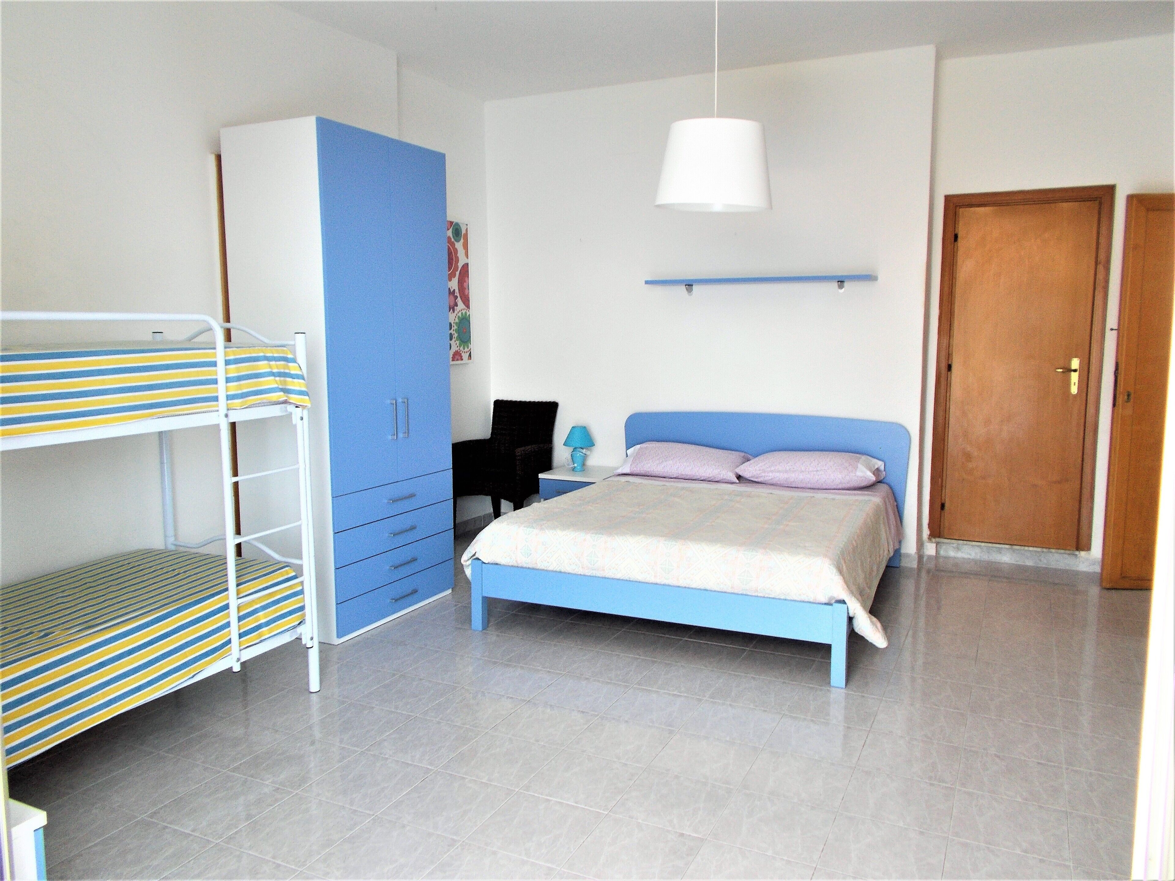 A bedroom with bunk beds, a wardrobe, a bed with a headboard, a nightstand, a lamp, and a door.