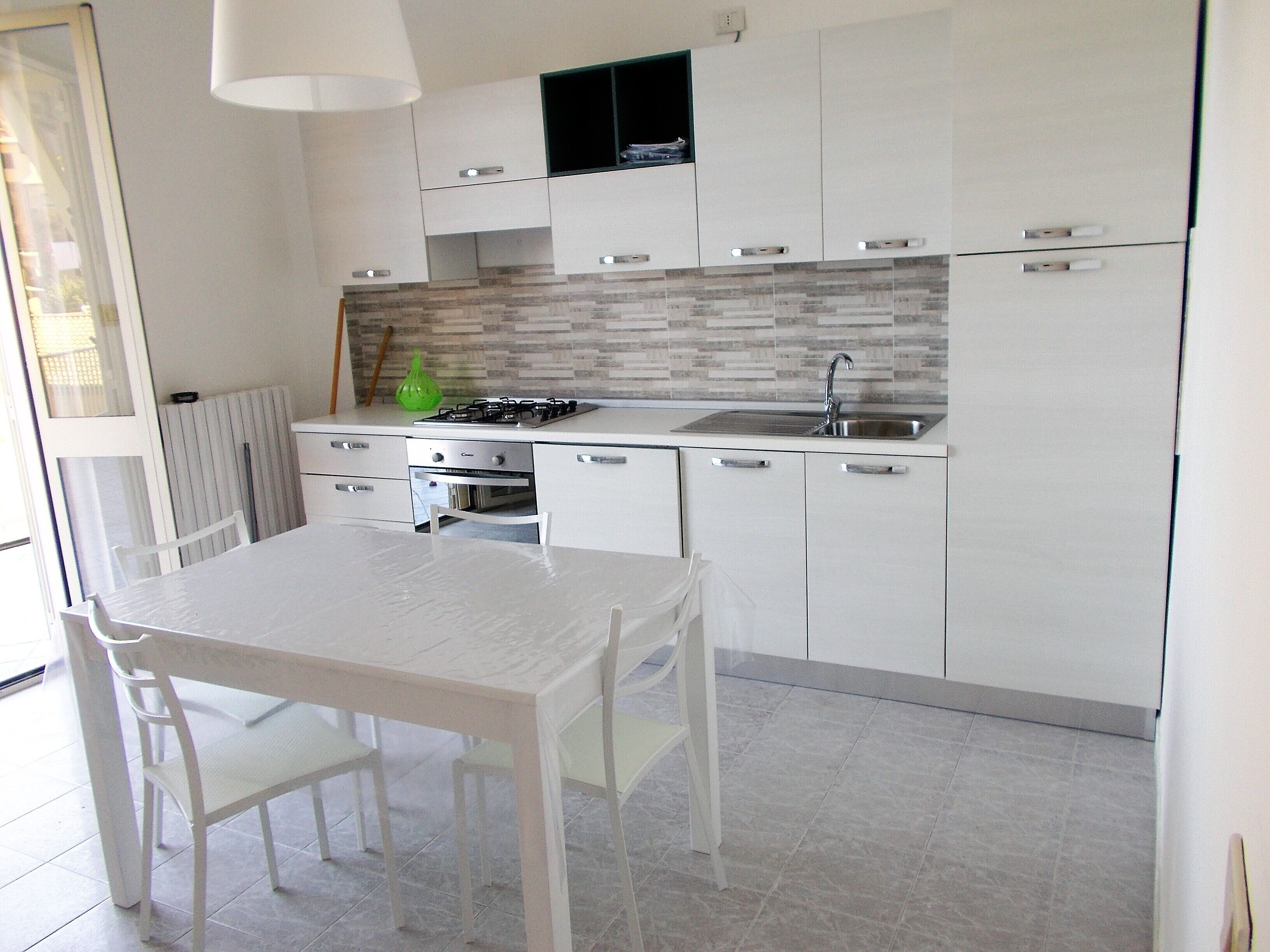 A modern kitchen with white cabinetry, a gas stove, and a sink. There is a dining table with chairs and a window providing natural light.