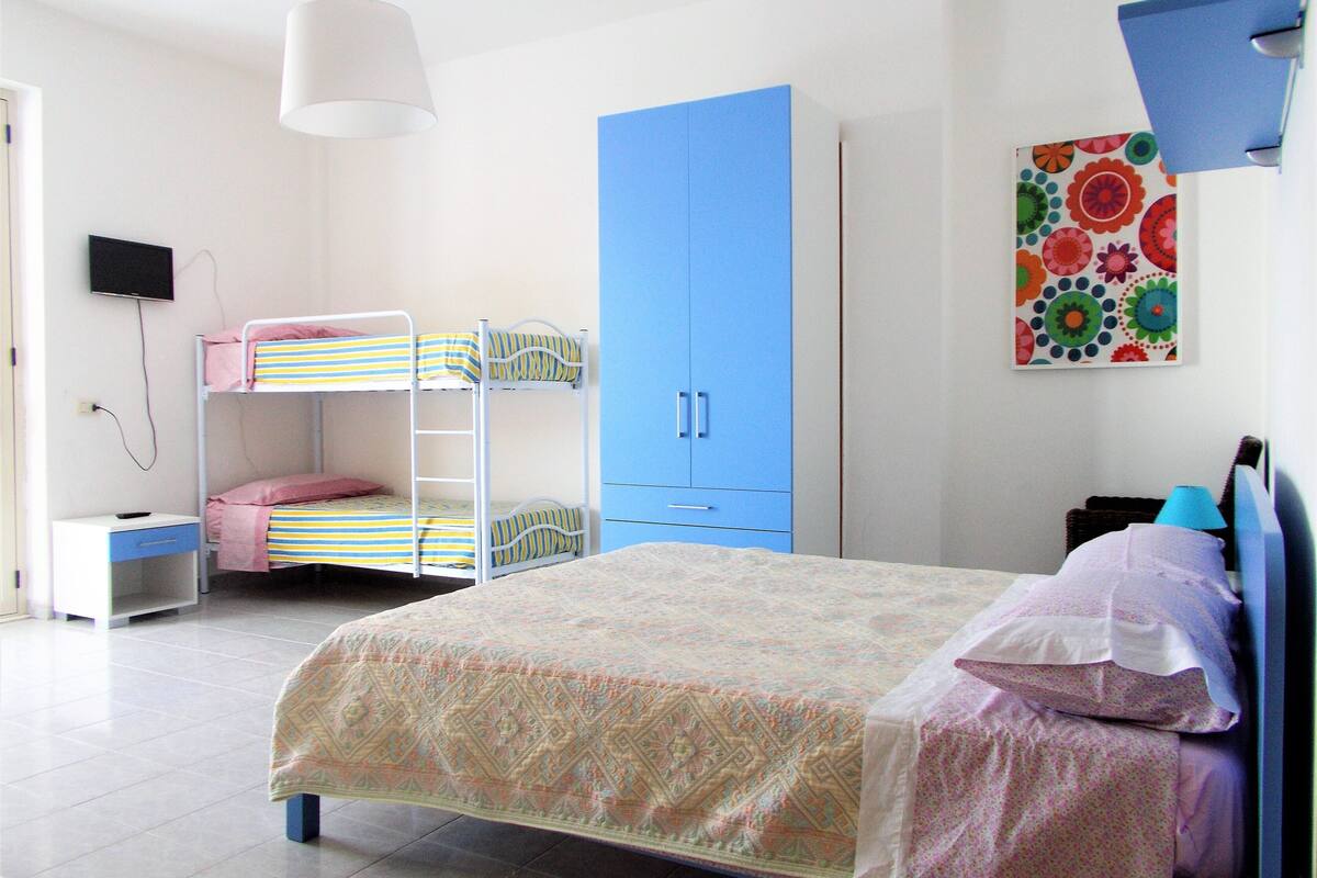 A bedroom with bunk beds, a desk, a wardrobe, and a bed with a patterned bedspread.