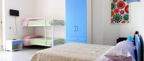 A bedroom with bunk beds, a desk, a wardrobe, and a bed with a patterned bedspread.