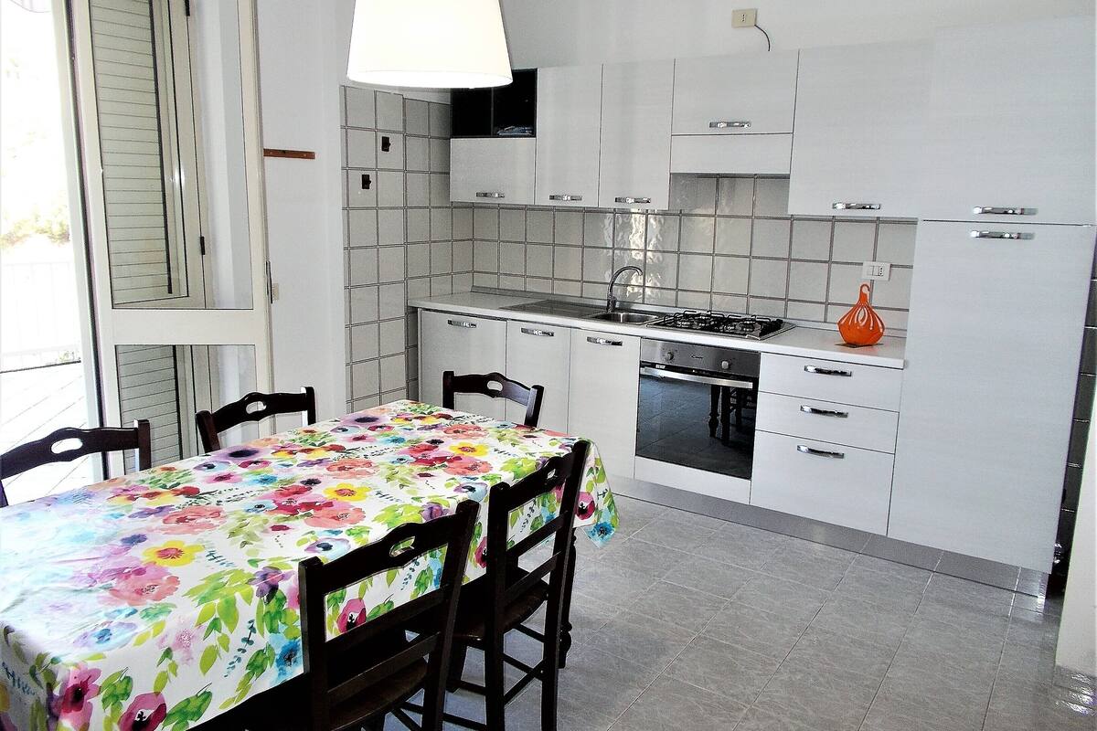 A kitchen with white cabinets, a gas stove, and a table with a floral tablecloth.