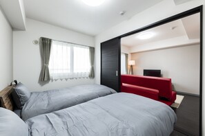 A hotel room with two beds, a red sofa, a desk with a lamp, and a television. - STELLAR 605 (Sapporo)