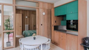 A compact kitchen with wooden cabinetry, a dining table, and a small coffee machine. - Designer 1BR Soho Apt | AC | Heart of West End (London)