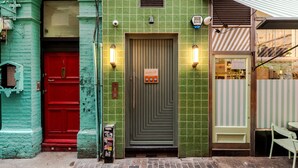 A building with a green tiled facade, a red door, and a storefront with striped awnings. - Designer 1BR Soho Apt | AC | Heart of West End (London)