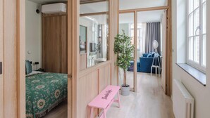A room with a bed, a bench, a potted plant, and a view of another room through a mirrored wall. - Designer 1BR Soho Apt | AC | Heart of West End (London)