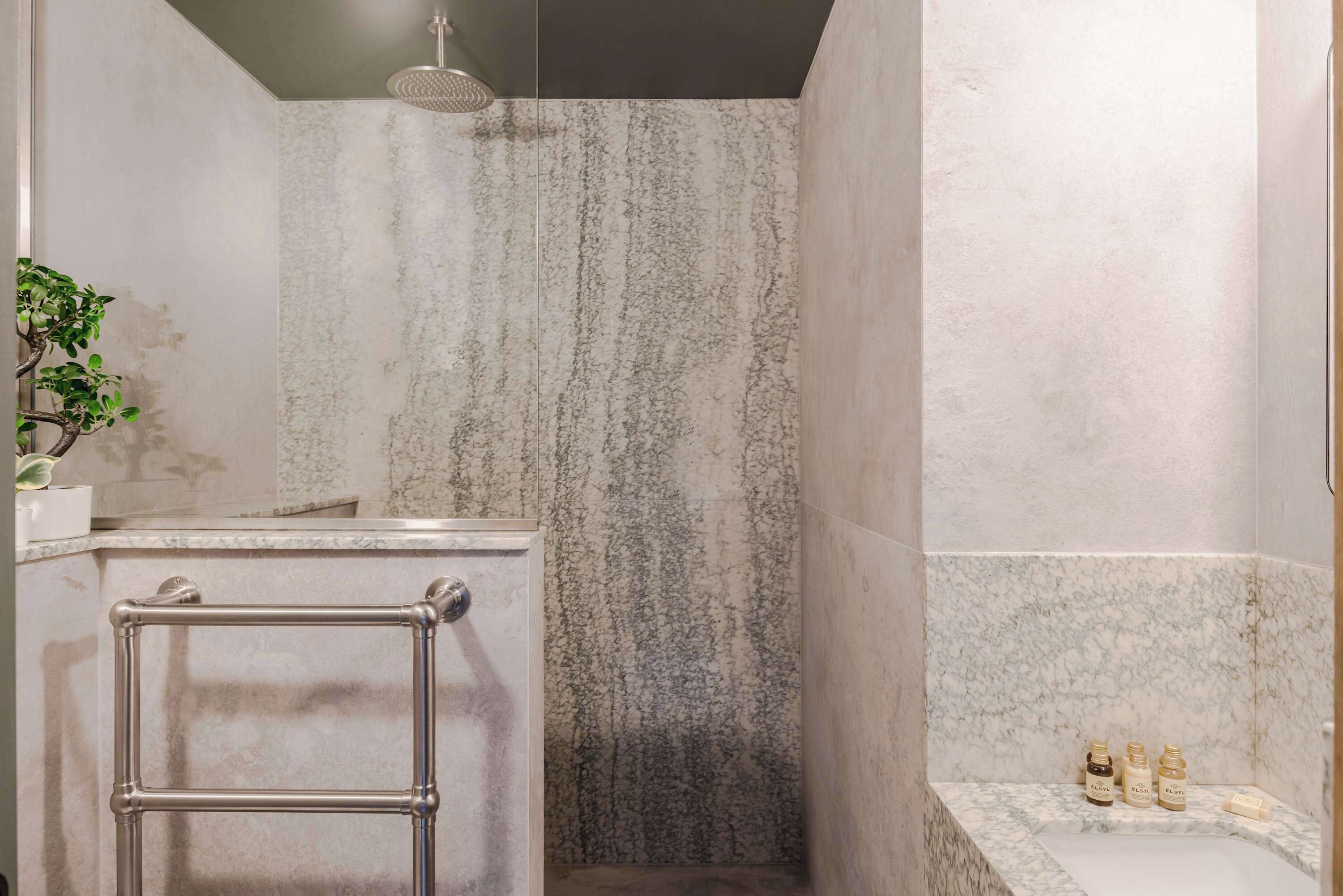 A bathroom with a marble shower, a towel rack, and toiletries on the counter.