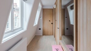 A narrow hallway with a wooden door, a radiator, and a pink bench with text. - Top-Floor Soho Flat | AC | Sleeps 4 | Central Ldn (Greater London)