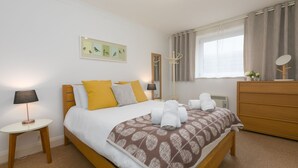 Een netjes ingerichte slaapkamer met een bed, nachtkastjes, een kaptafel en een raam met gordijnen.