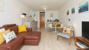 Een moderne woonkamer met een bruine leren bank, een eettafel met stoelen, een tv-meubel en een keuken op de achtergrond.