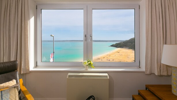 Een kamer met een groot raam met uitzicht op een strand, een radiator en een lamp op een tafel.