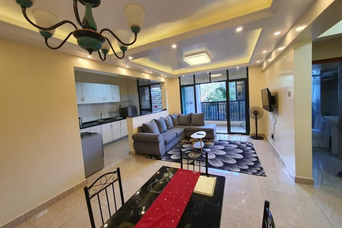 A modern living room with a sofa, a dining table, and a kitchen in the background.
