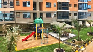 Une aire de jeux avec un toboggan et des structures d’escalade, entourée d’une pelouse bien entretenue et de plantes en pot.