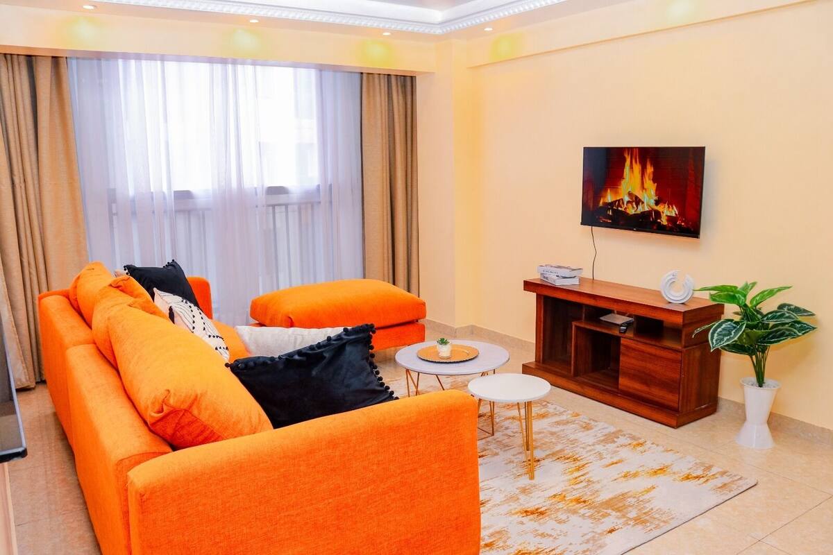 A modern living room with a sofa, ottoman, coffee table, TV, and a plant.