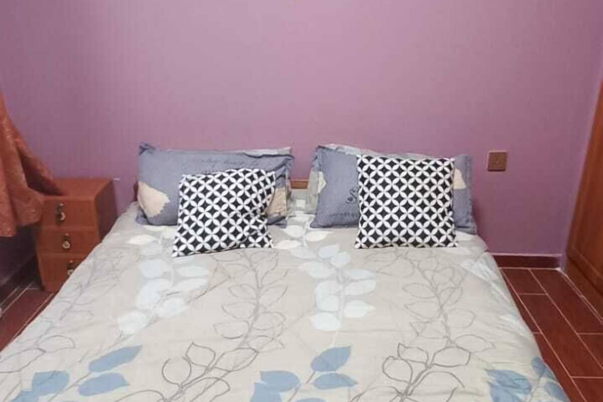 A bedroom with a bed, two pillows, a nightstand, and a wooden chair.