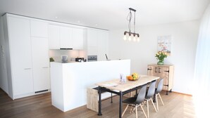 A modern kitchen with white cabinetry, a central island, and a dining area with a wooden table and chairs.