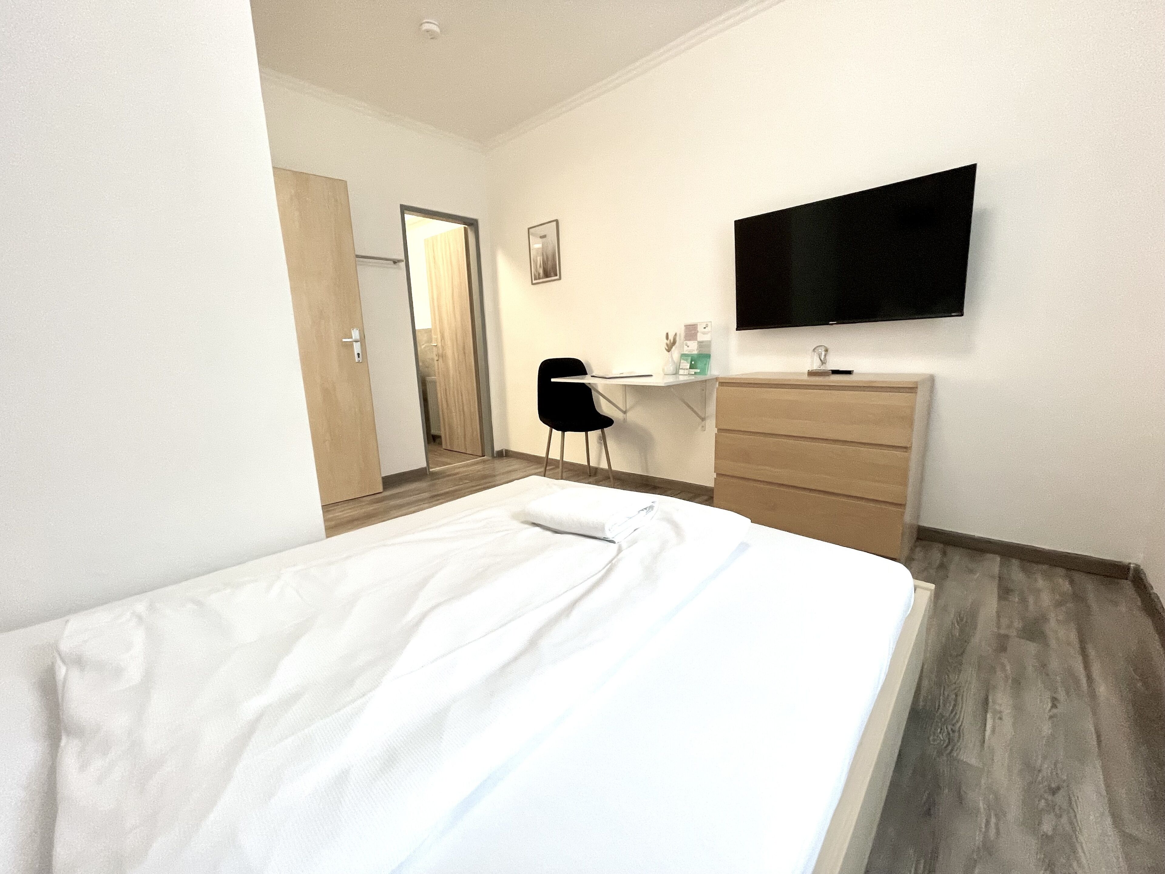 A hotel room with a bed, a desk, a chair, a dresser, and a TV mounted on the wall.