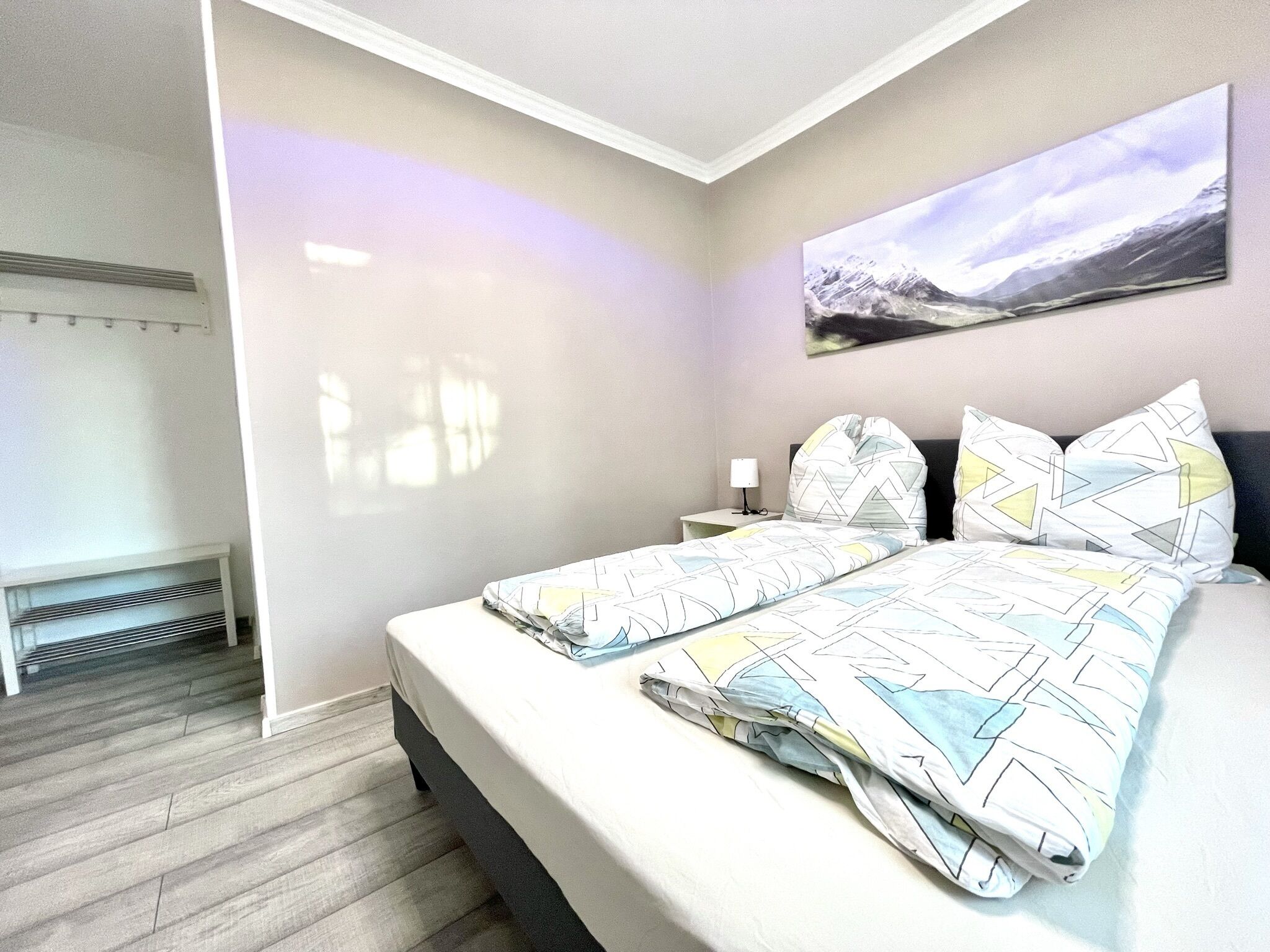 Ein modernes Schlafzimmer mit Bett, Nachttisch, Wandlampe und einem großen Fenster.