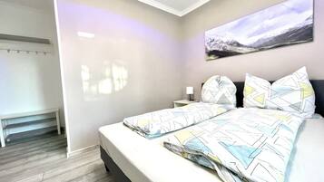 Ein modernes Schlafzimmer mit Bett, Nachttisch, Wandlampe und einem großen Fenster.