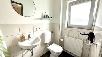 A bathroom with a white sink, toilet, and a mirror. There is a window above the toilet and a radiator below it.