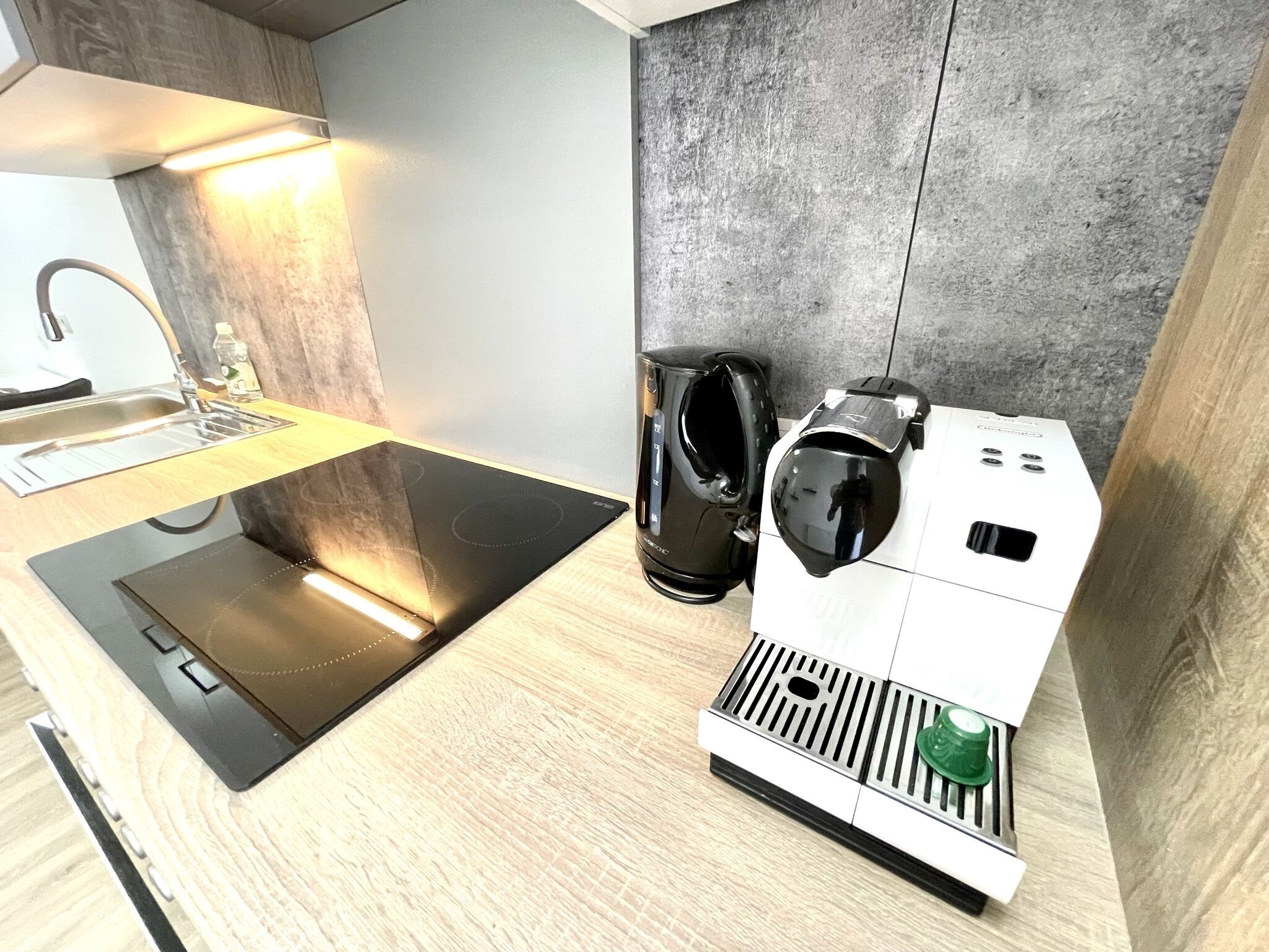 Une cuisine moderne équipée d’une plaque de cuisson intégrée, d’une machine à café et d’un évier.