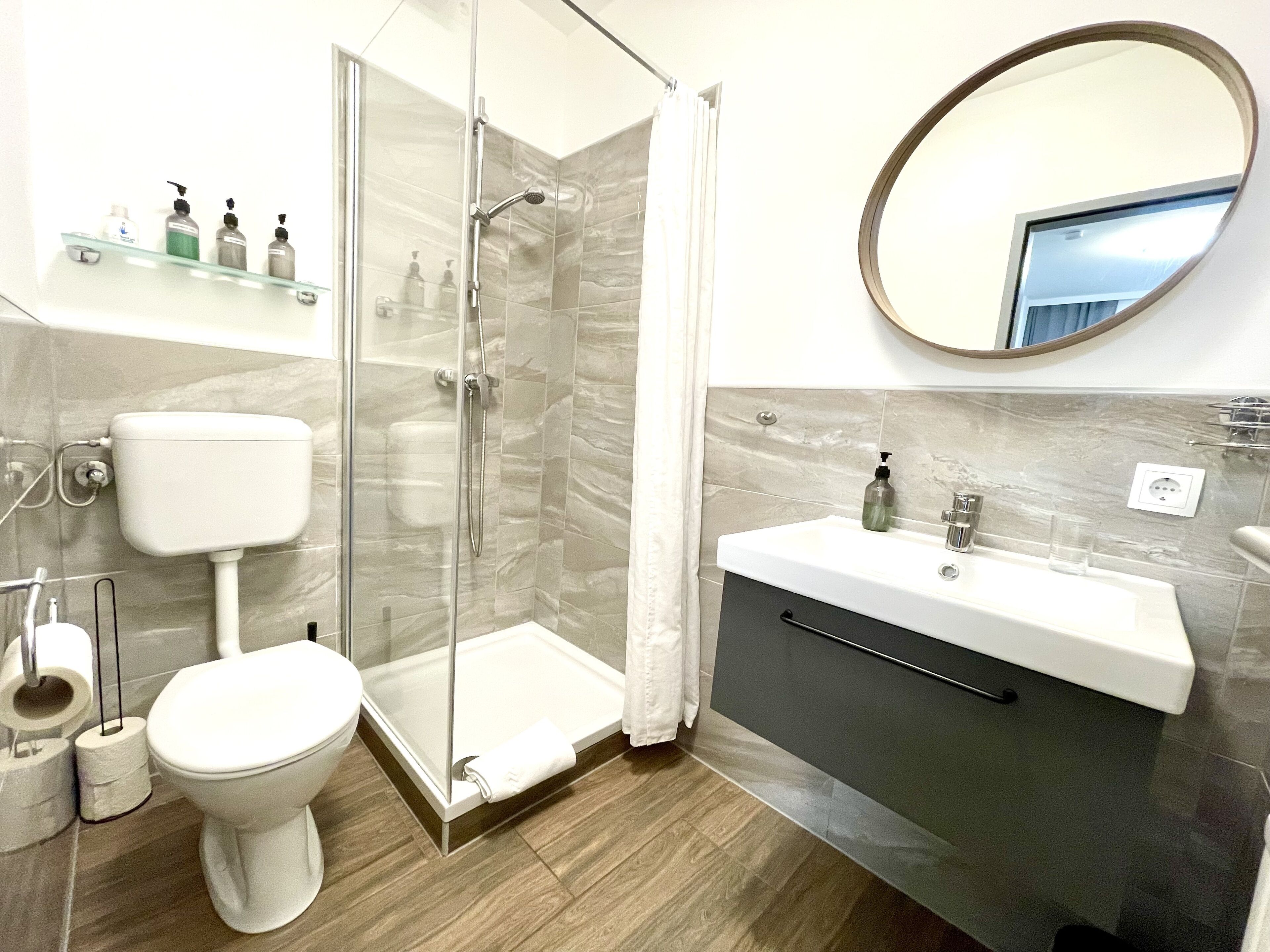A modern bathroom with a glass-enclosed shower, a toilet, a sink with a mirror, and toiletries on a shelf.